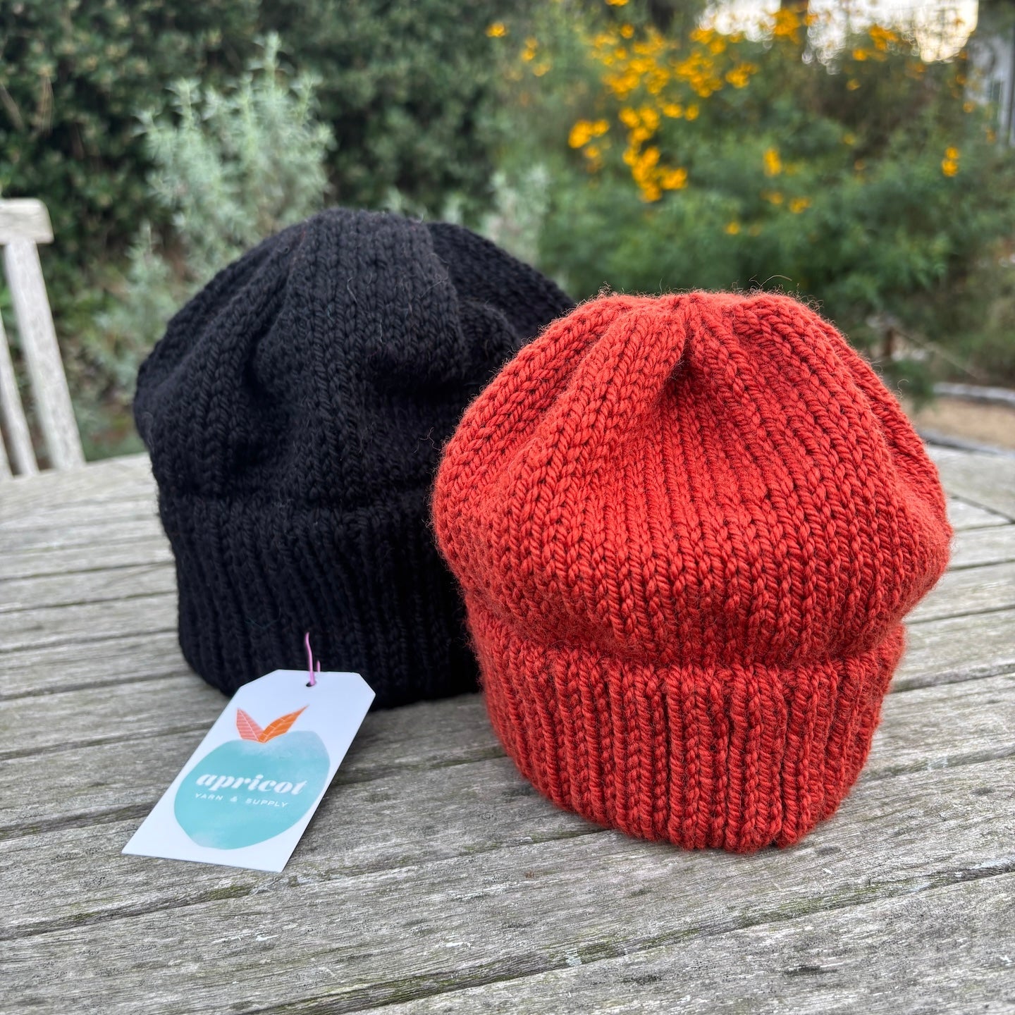 Two knit hats, one black and one red, on a wooden surface with a blurred natural background.