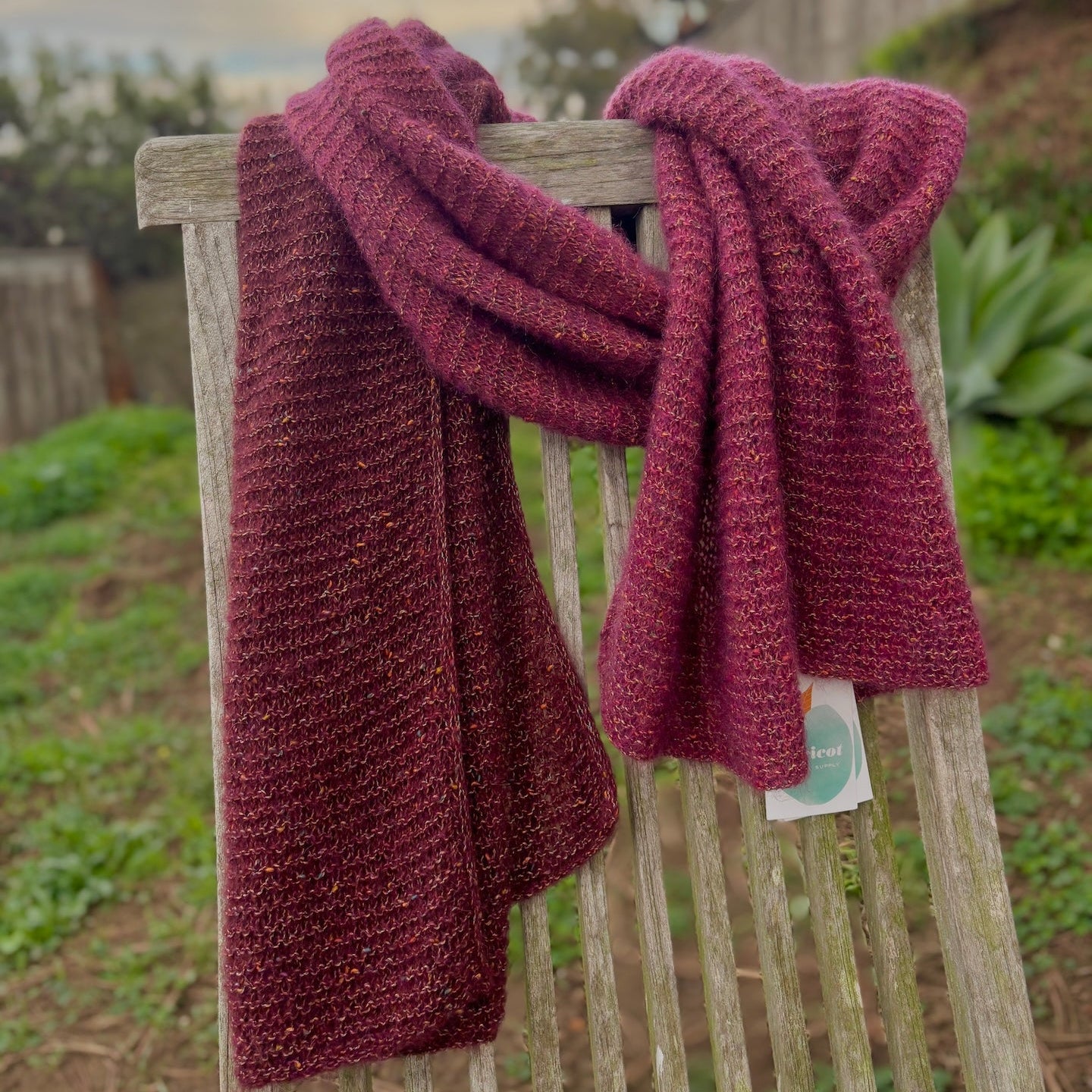 Maroon knitted scarf draped over a wooden chair outdoors with a garden background