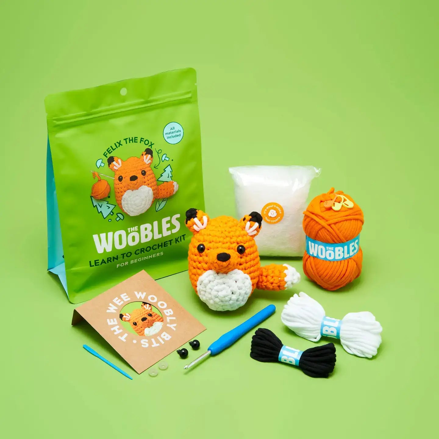 Crochet kit with fox-themed packaging, yarn, and tools on a green background from the The Woobles Kits collection by Apricot Yarn & Supply