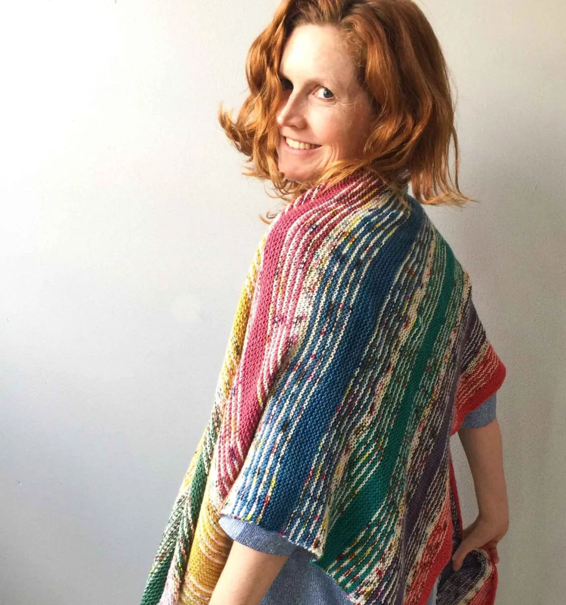 Woman wearing a colorful knitted shawl against a plain background