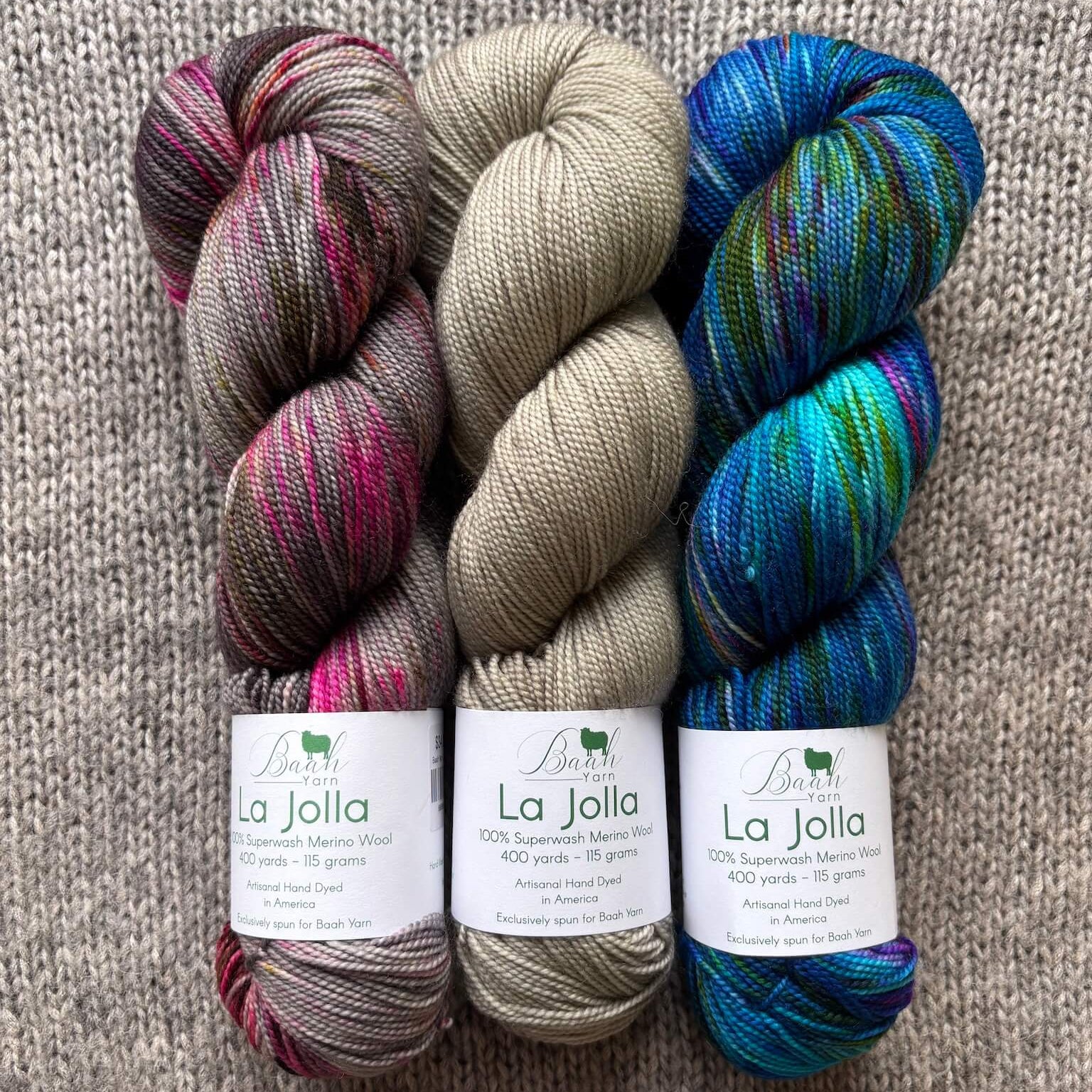 Three skeins of yarn in different colors with labels on a textured surface