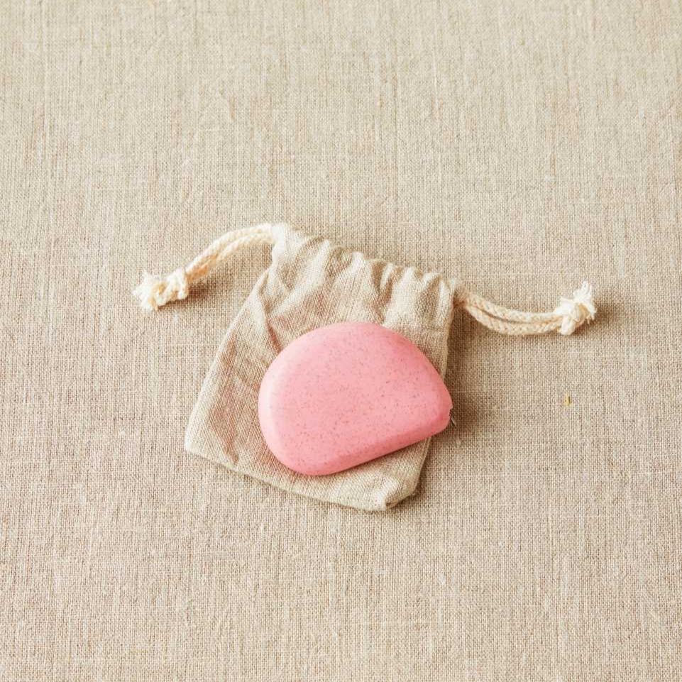Pink stone in a small drawstring bag on a beige fabric background