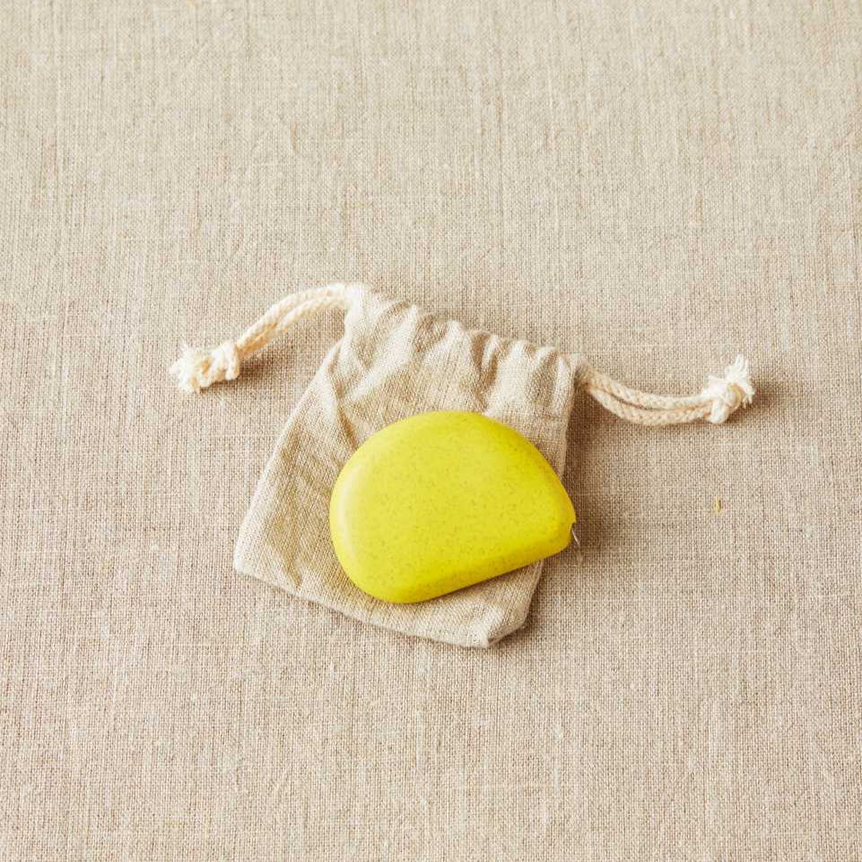 Yellow measuring tape in a small white drawstring bag on a beige fabric background