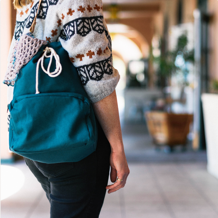Woman in an exterior hall with a deep teal canvas bag over her shoulder