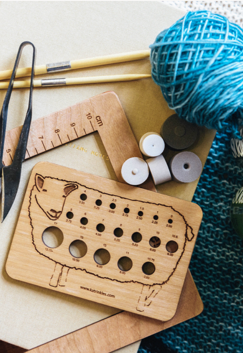 Wooden knitting needle gauge with yarn and needles on a textured surface